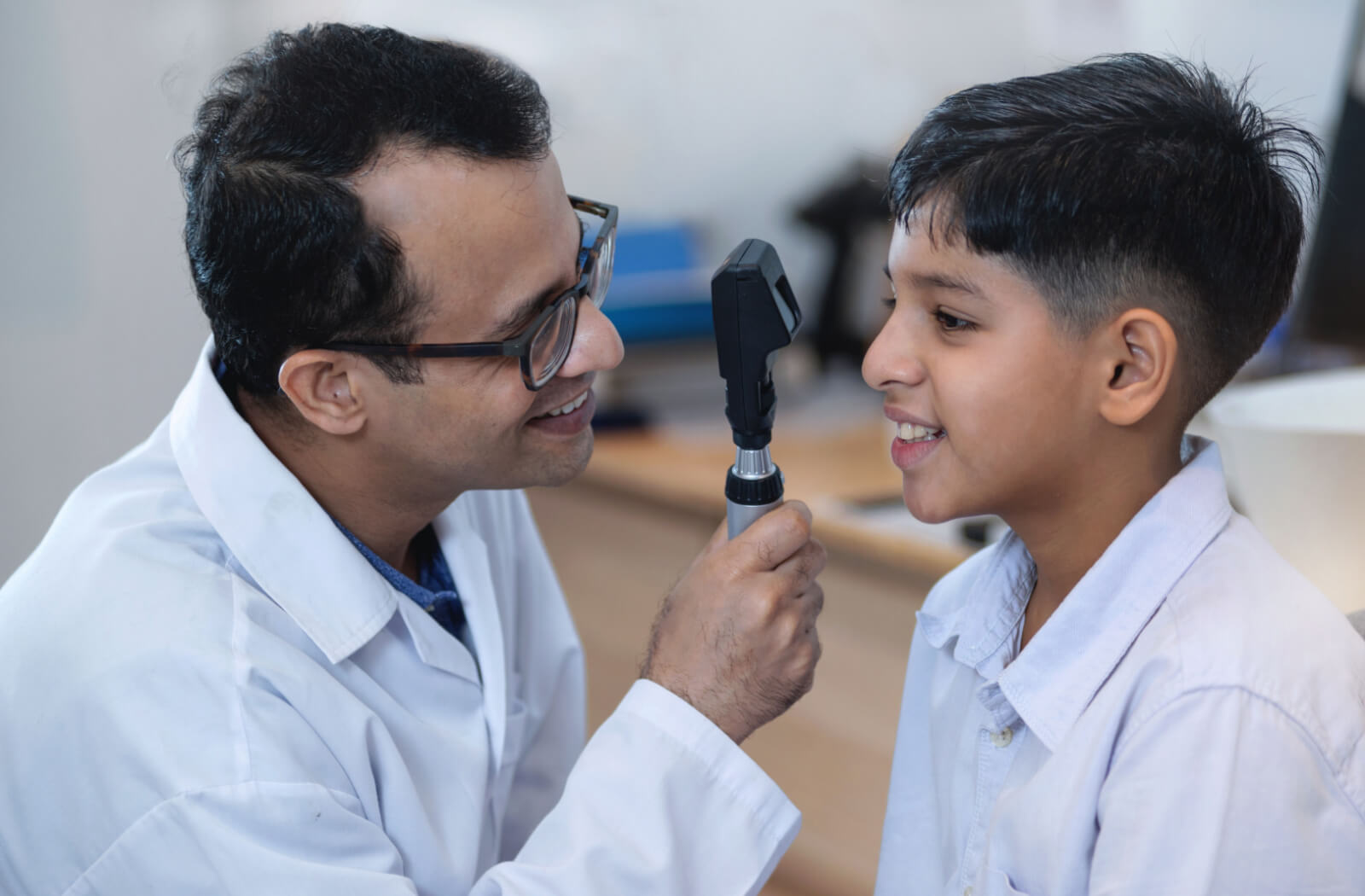 A smiling optometrist conducting an eye exam on a boy using a device to look into the boy's eyes.