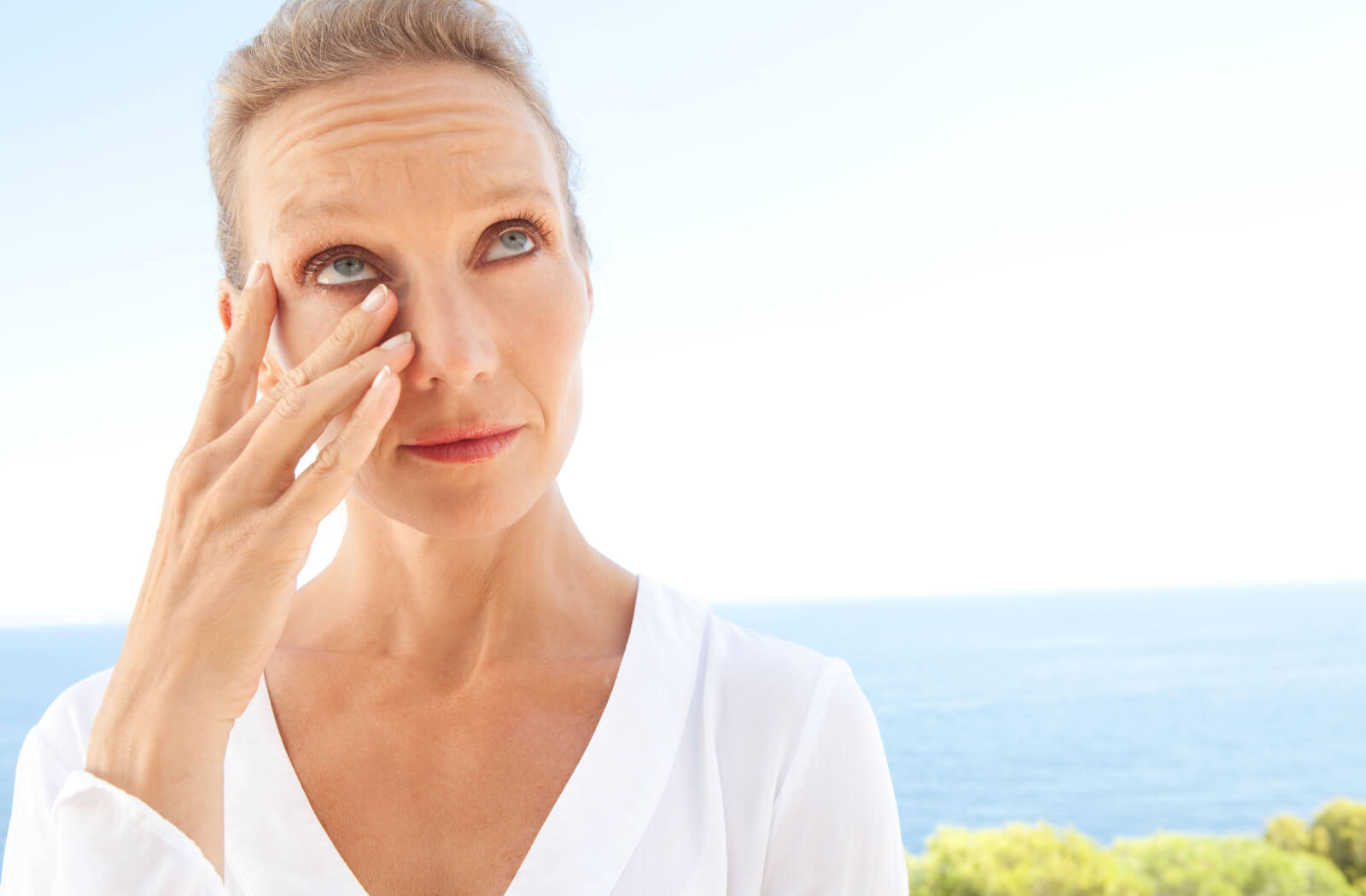 A woman  in a white blouse is scratching her red irritated dry eyes