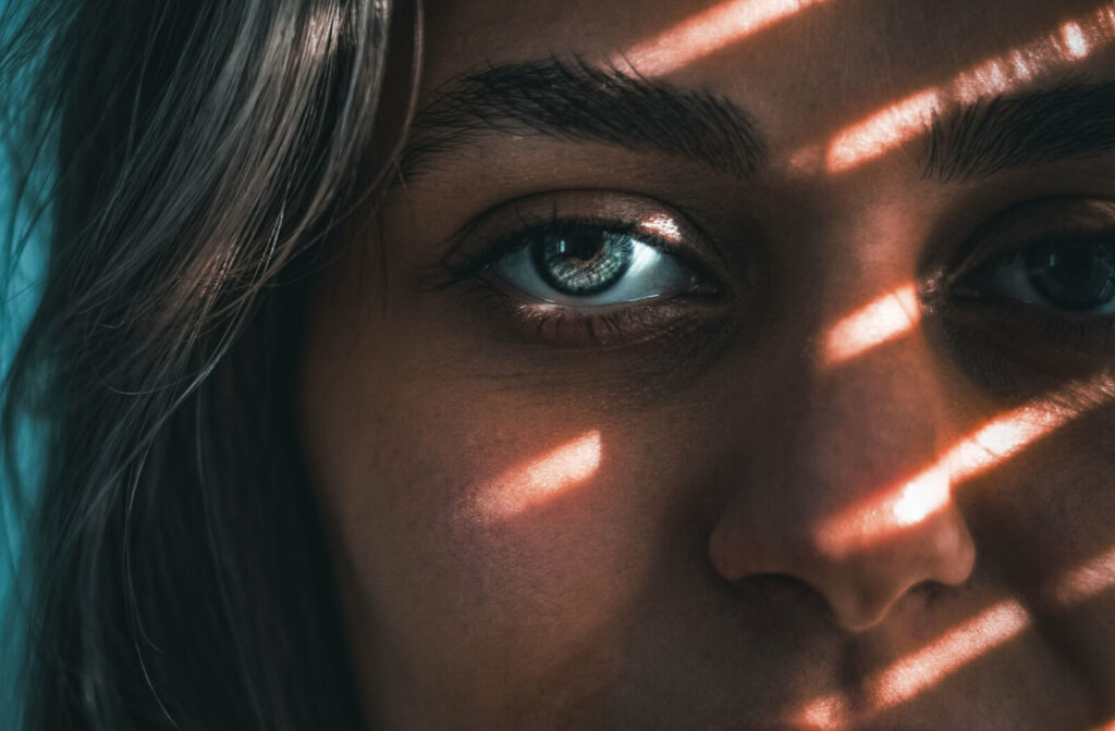 A portrait of a young female with blue eyes under blinds shadows, who is trying to escape sunlight
