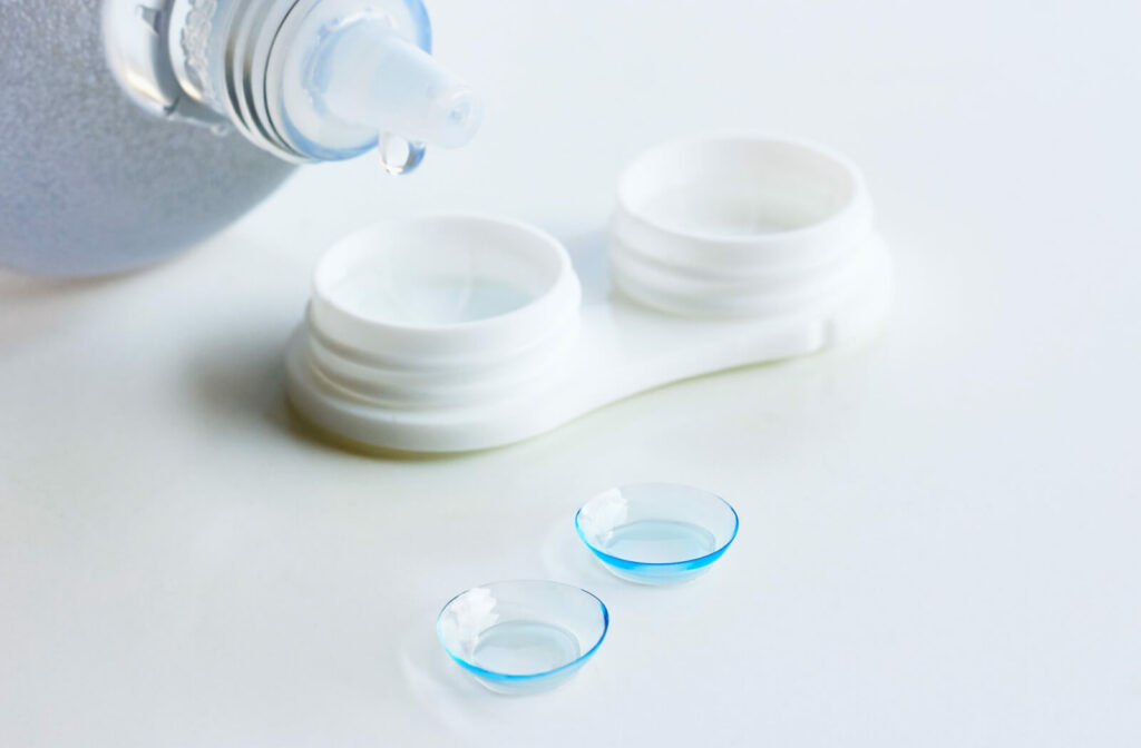 A pair of contact lenses beside a contact lens case and a bottle of contact solution.