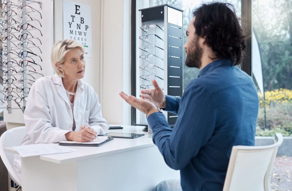 An optometrist taking notes and listening carefully as a patient describes their recent dry eyes and headaches.