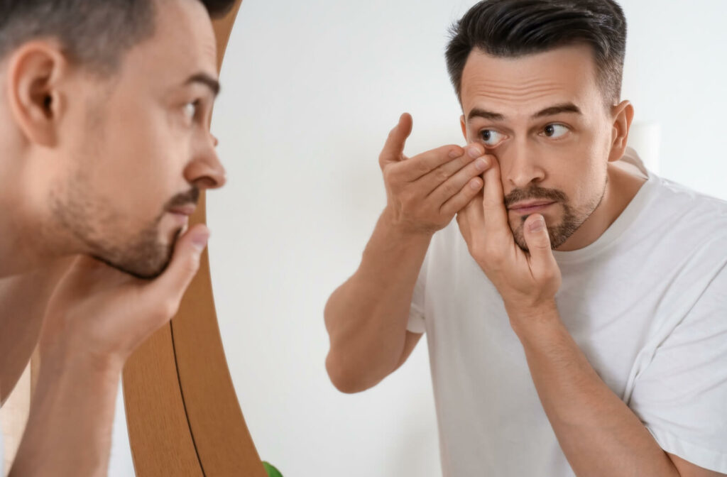Person standing in front of a mirror inserting a contact lens into their right eye.