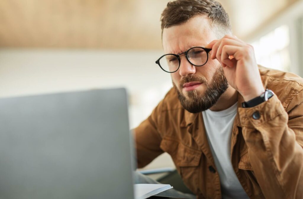 Person squinting while wearing glasses and looking at a laptop screen, suggesting difficulty seeing clearly or possible eye strain.
