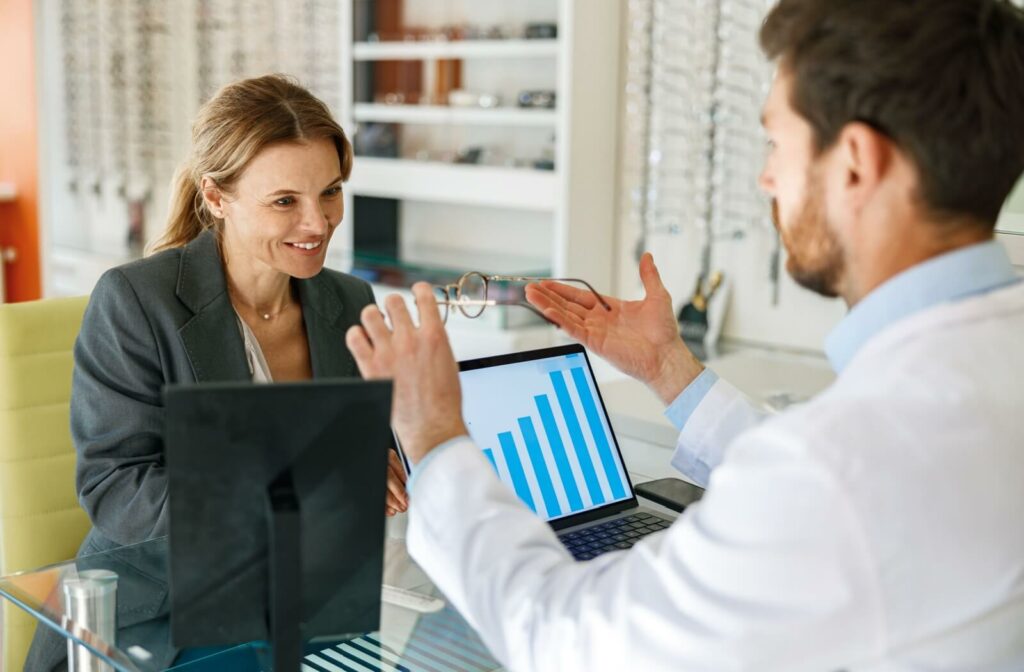 Optician showing a pair of eyeglasses to a smiling patient during a consultation, explaining the benefits of corrective lenses.