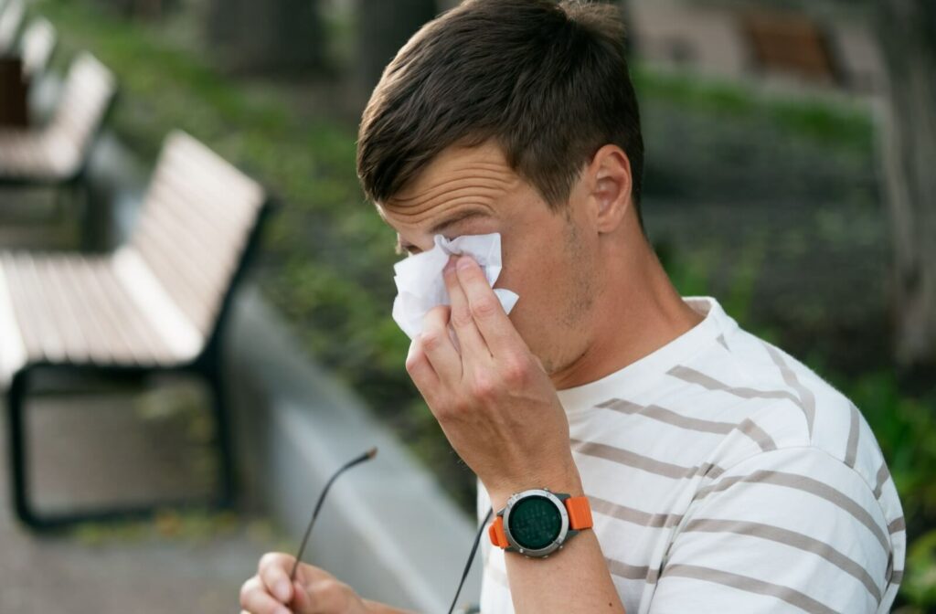 Person on a park bench wiping eye with tissue after taking off glasses