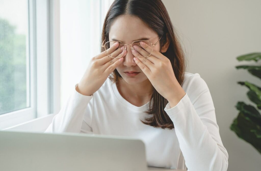 Person experiencing blurry vision and eye strain while working on a laptop, illustrating common causes of blurry eyesight such as digital eye strain and vision fatigue.
