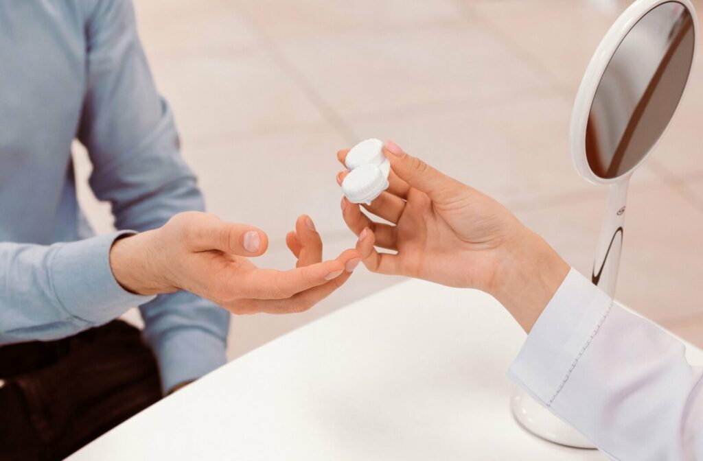 An eye care professional handing a white contact lens case to a patient during a vision consultation.