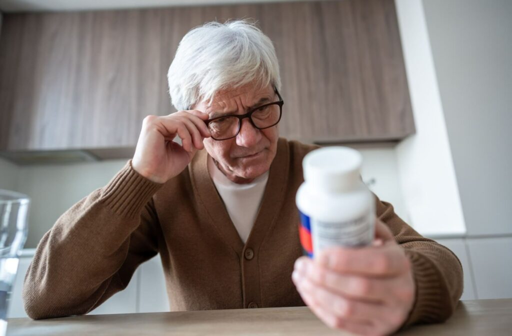 A senior man wearing glasses and squinting to read a medicine bottle label, illustrating central vision challenges from wet AMD.