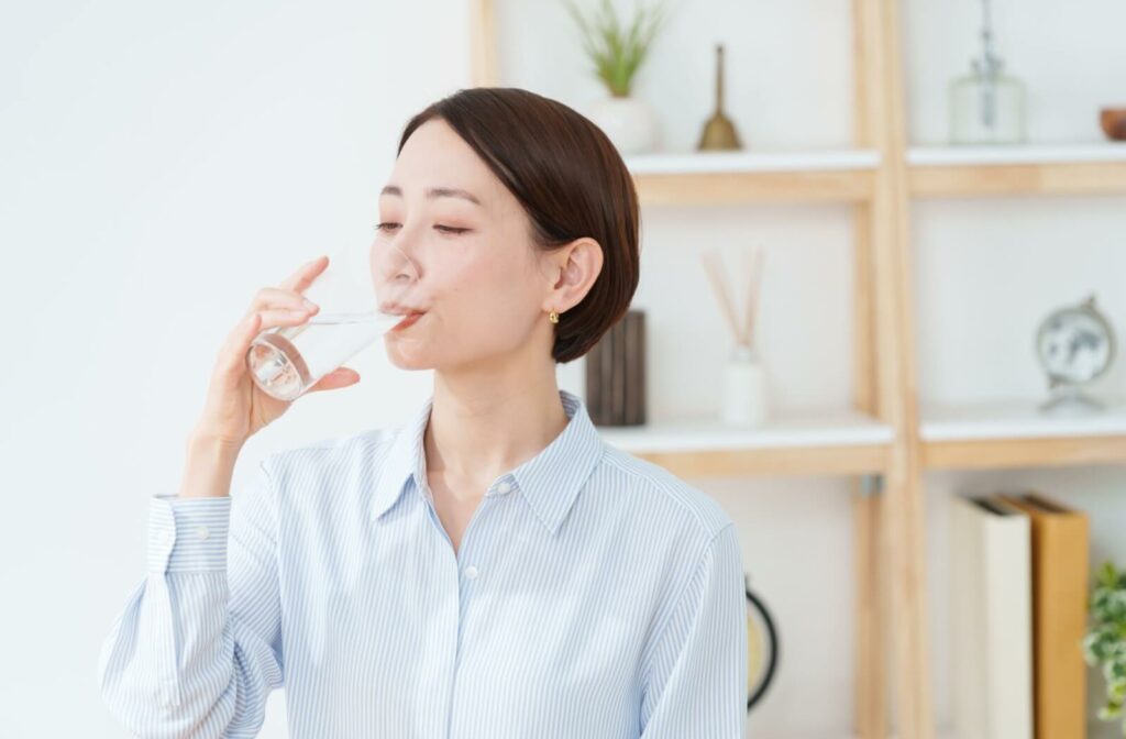 A woman with clear skin drinking a glass of water, highlighting the importance of hydration for skin healing and health.